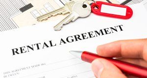A Rental Agreement being signed with a red pen, and two keys on a red and white keyring