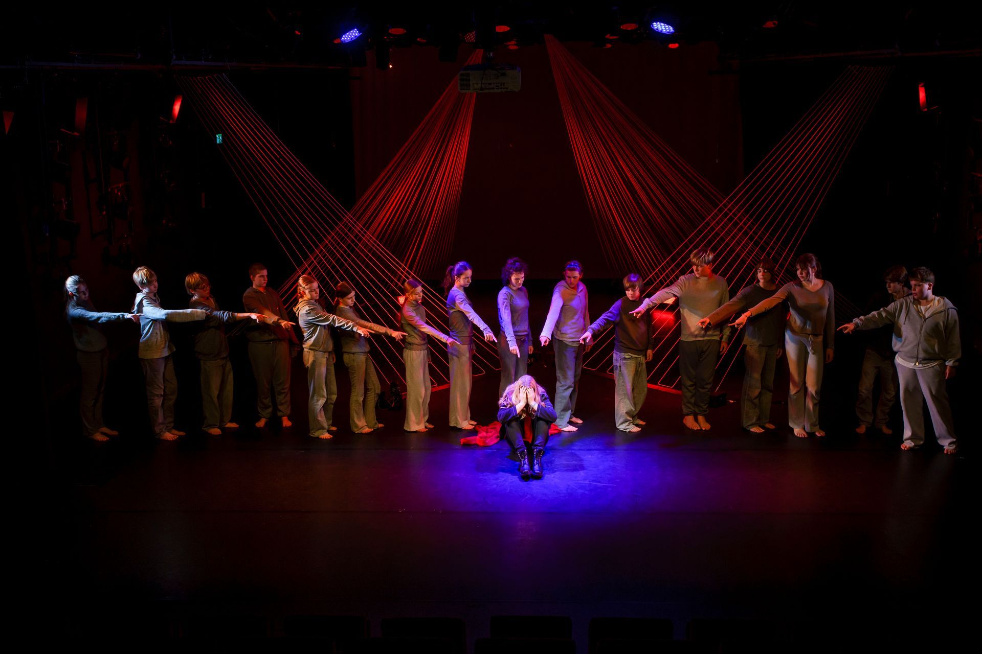 Een groep mensen staat in een rij, met hun armen uitgestrekt naar een persoon in het midden, het podium verlicht door rode lichtstralen.