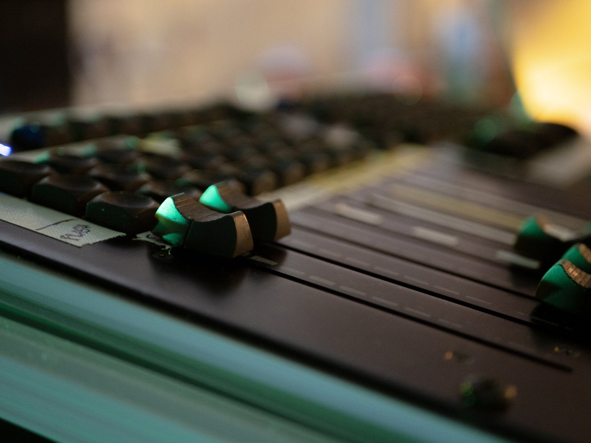 Close-up van een zwarte dmx lichtcontroller met groen verlichte faders en knoppen.