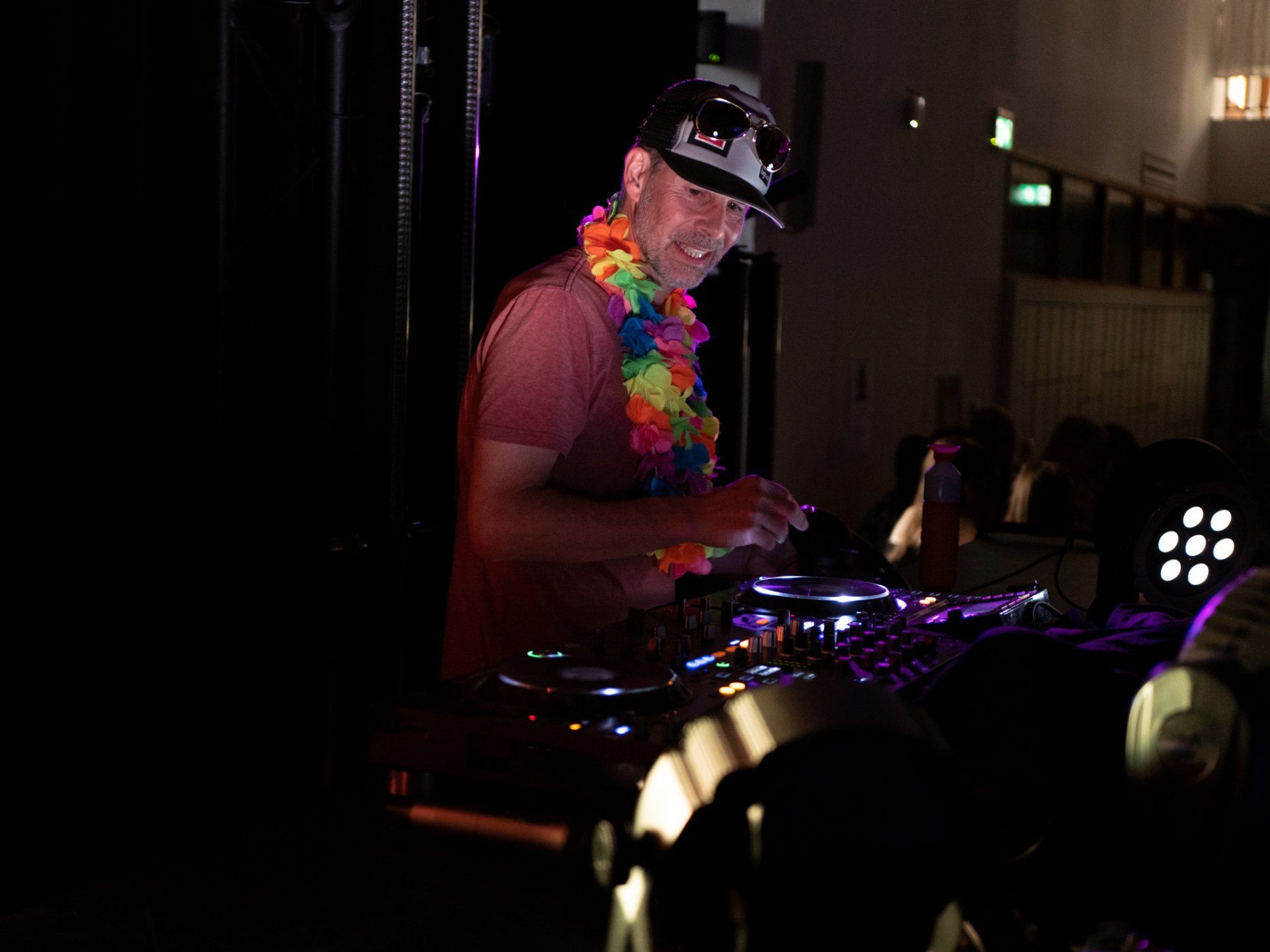 Een dj met een bloemenkrans en een baseballpet draait muziek tijdens een evenement in het donker.