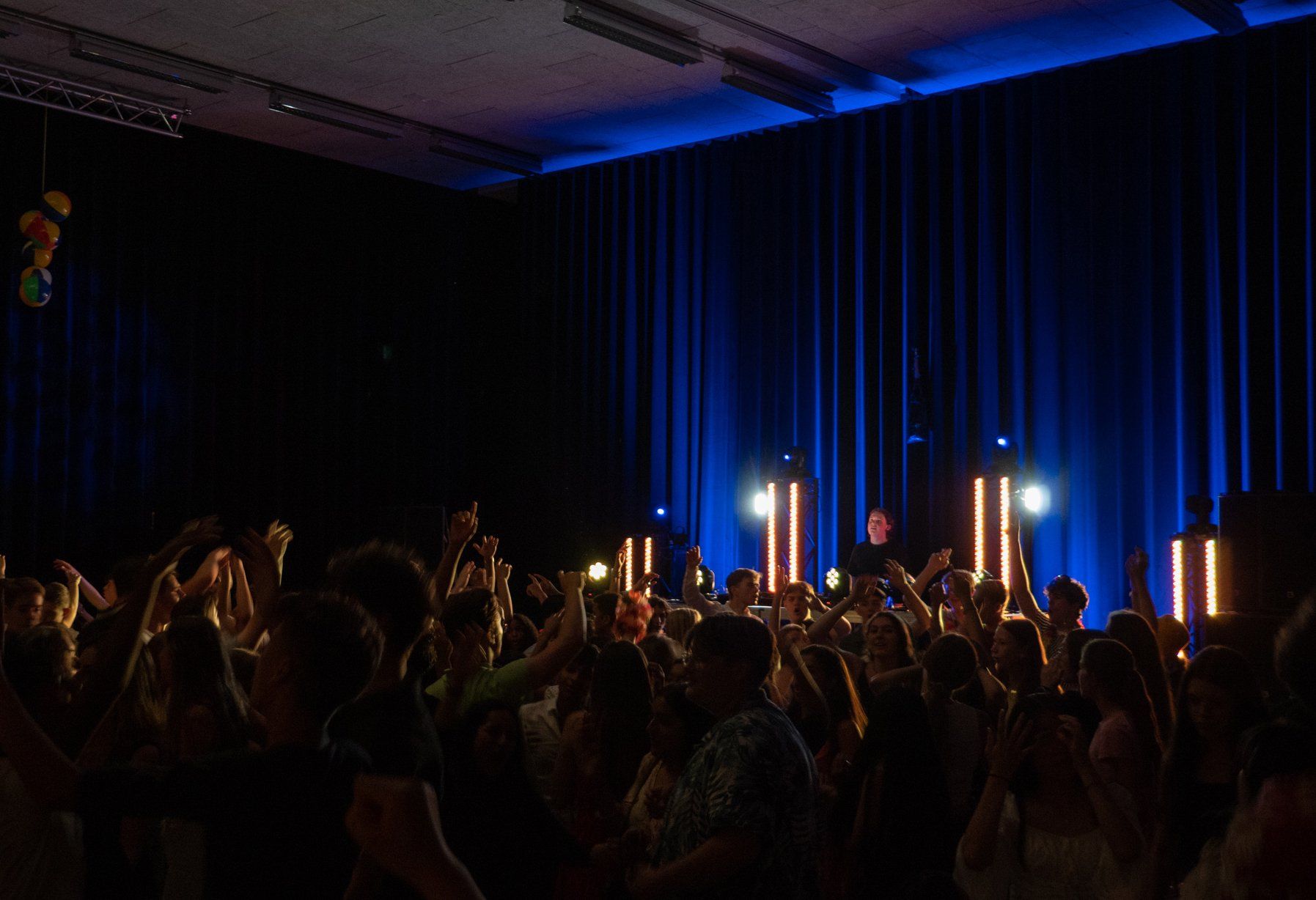 Mensen dansen op een concert met blauwe podiumverlichting en verticale lichtzuilen.