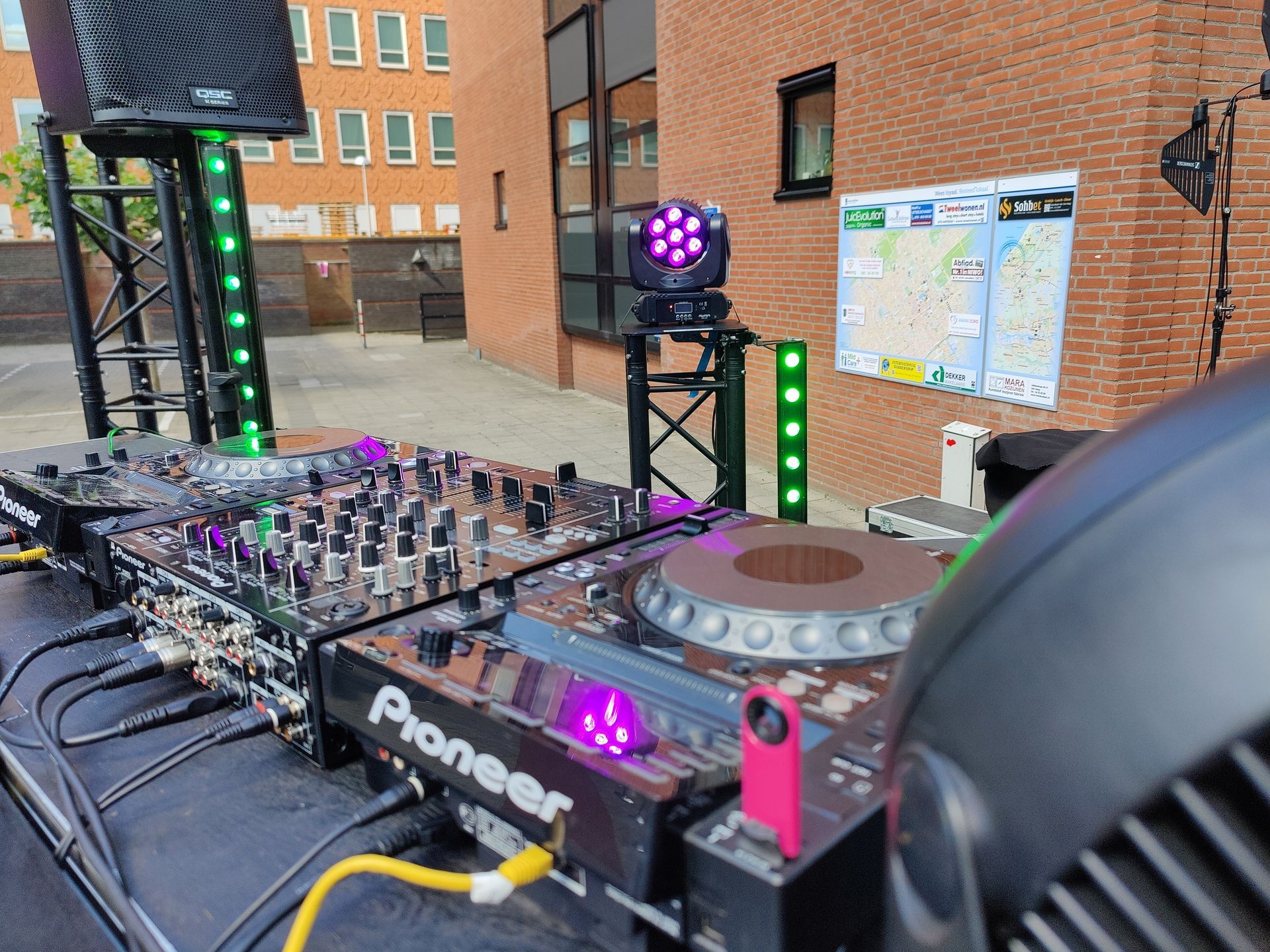 DJ-setup buiten met Pioneer-apparatuur, speakers en podiumverlichting.