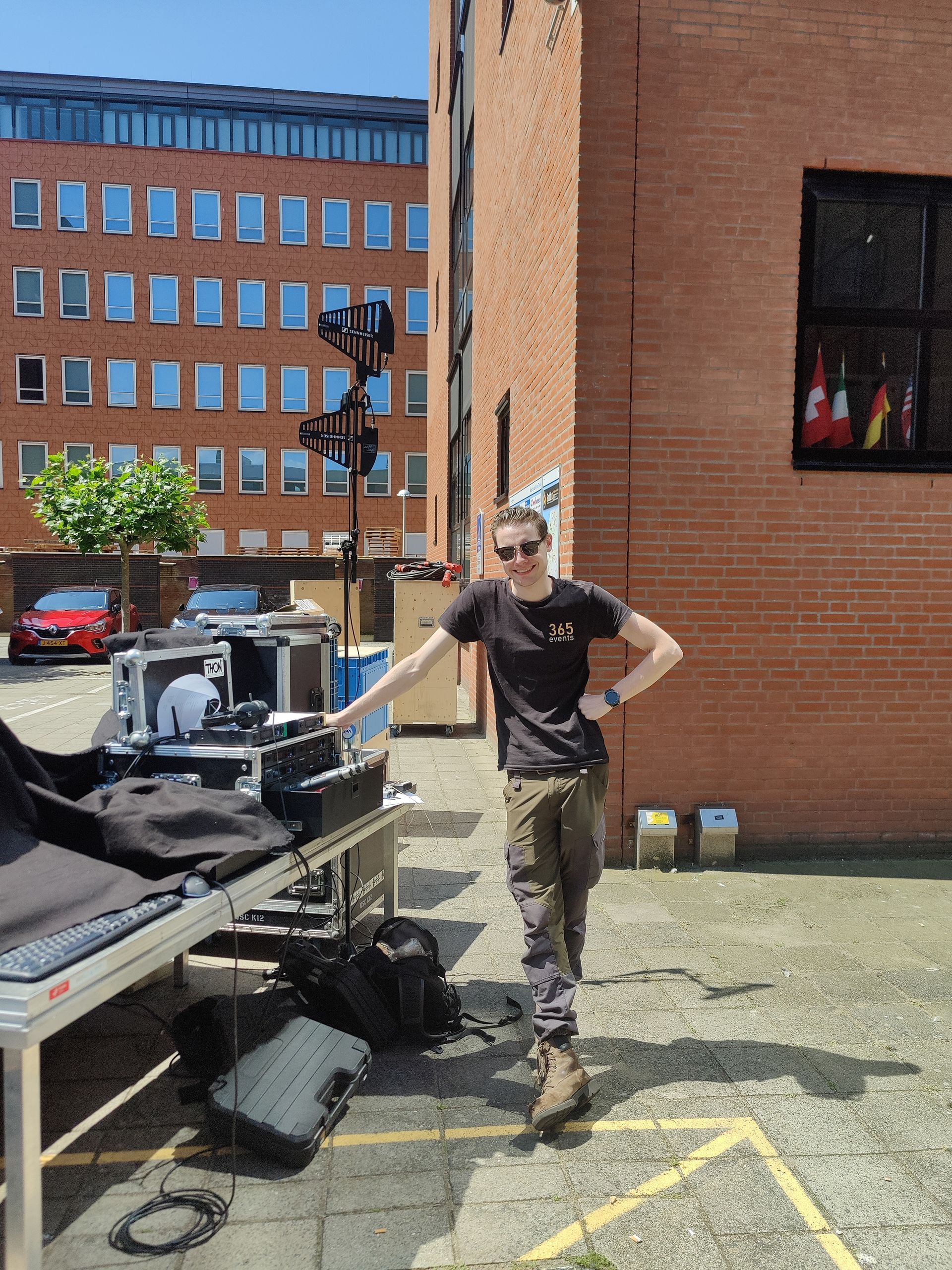 Een man staat bij geluidsapparatuur die buiten voor een bakstenen gebouw is opgesteld.