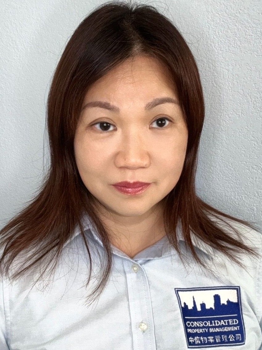 A woman with long brown hair is wearing a white shirt and looking at the camera.