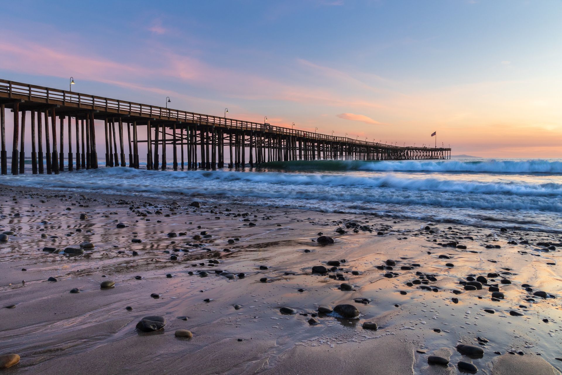 There is a pier on the beach at sunset.
