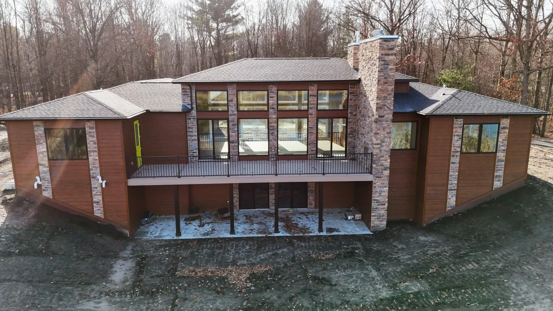 Front view of a brick house with large windows, a covered porch, and a chimney in a wooded setting