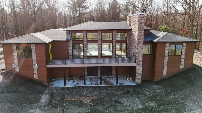 Brick house with large windows, front porch, and snow-dusted roof in a wooded yard