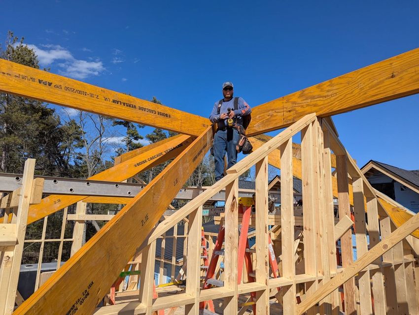 Construction worker standing on roof trusses at a house under construction, with bright blue sky overhead