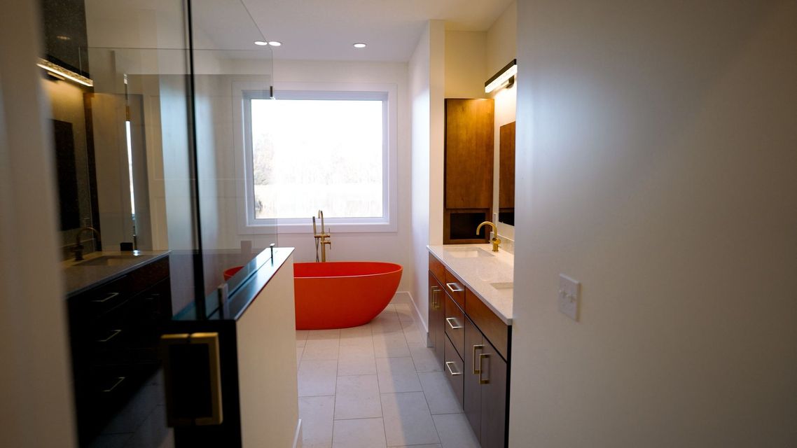 Modern bathroom with a red bathtub, vanity sinks, and a bright window at the far end