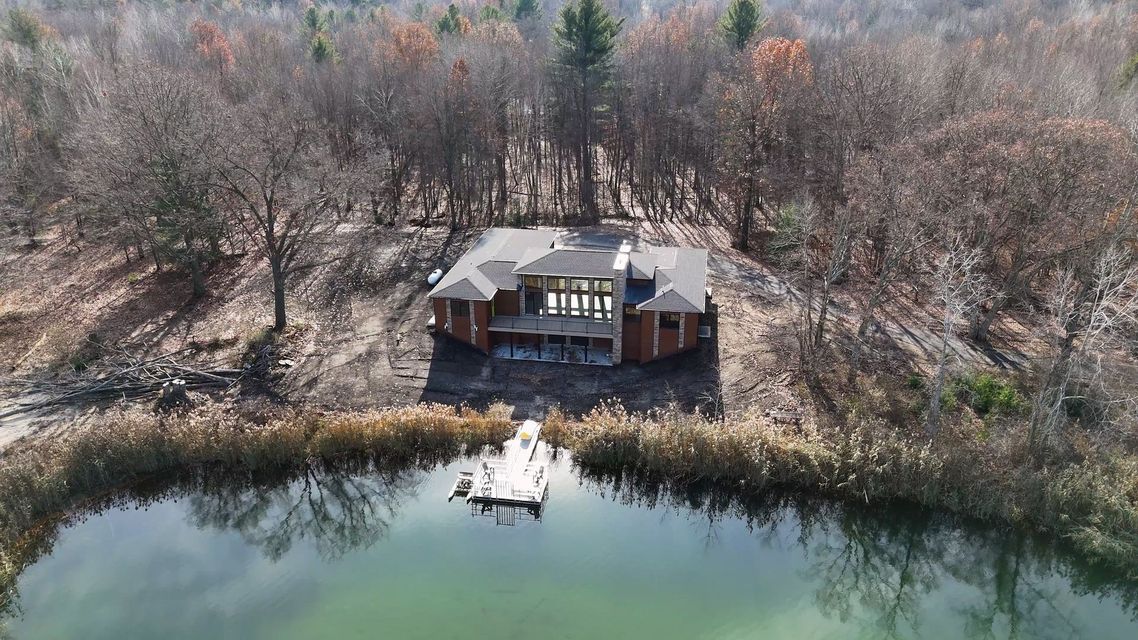 Aerial view of a lakeside cabin with a dock, surrounded by bare trees and calm water.