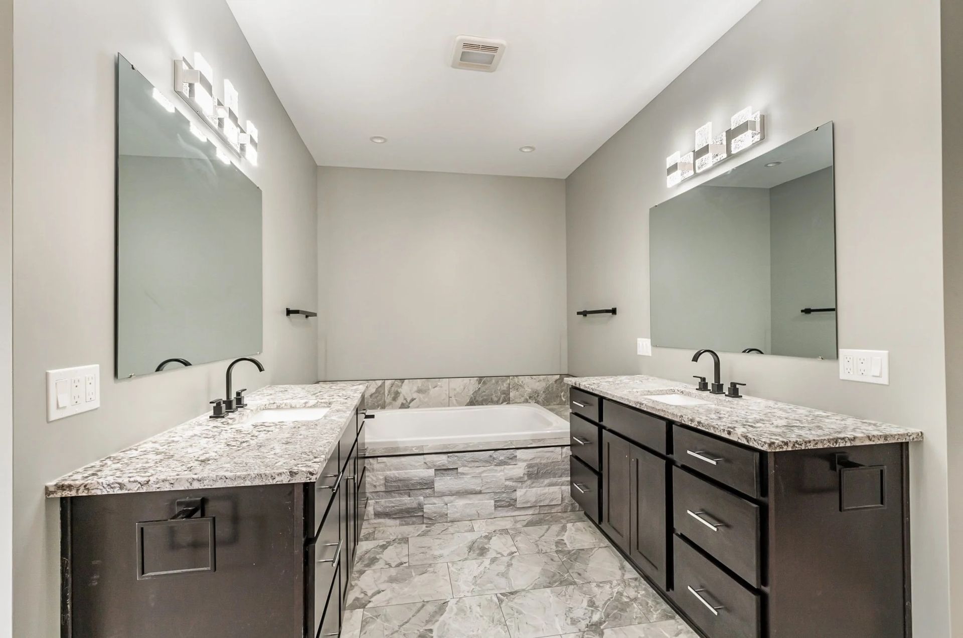 Modern bathroom with double sinks, large mirrors, gray walls, and marble countertops and flooring