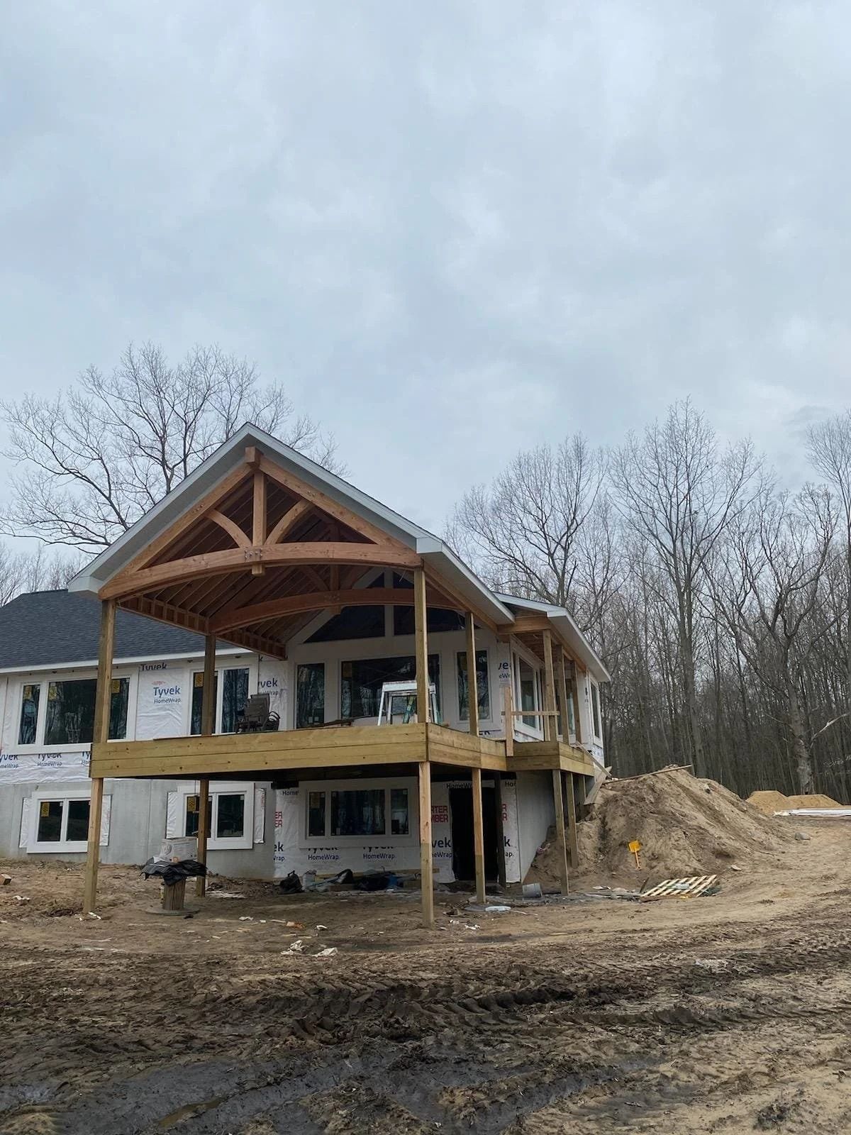Partially built two-story house with exposed wood framing and dirt piles on a cloudy day