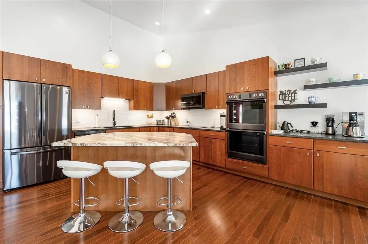 Modern kitchen with wood cabinets, stainless appliances, island stools, and hardwood floors