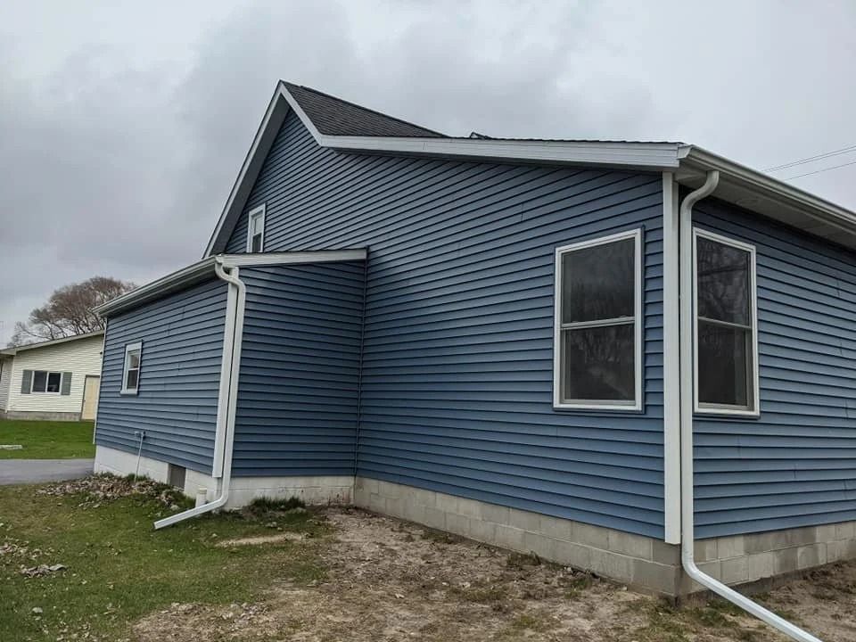 Blue vinyl-sided house with gray foundation and a small porch on a cloudy day