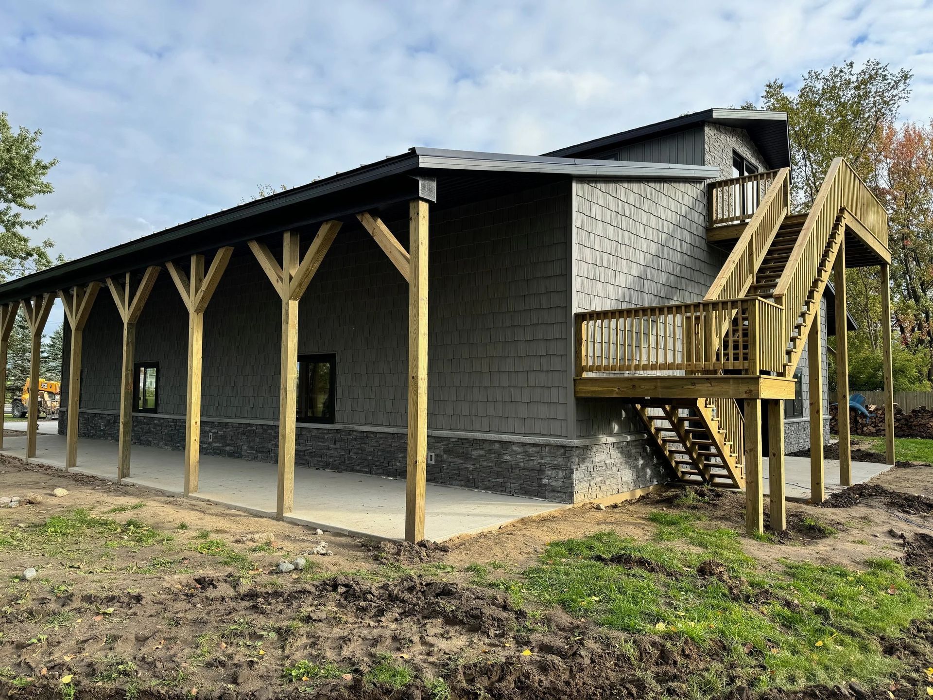 Dark gray house with a covered porch and wooden stairs, viewed from the side in a rural setting