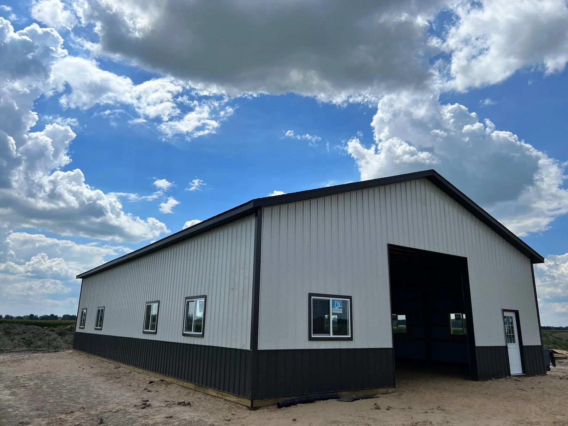 White metal barn with a black lower half and open doorway under a cloudy blue sky