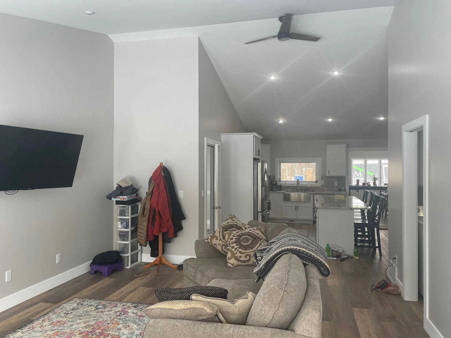 Living room with sectional sofa, wall-mounted TV, coat rack, ceiling fan, and open view to kitchen and dining area