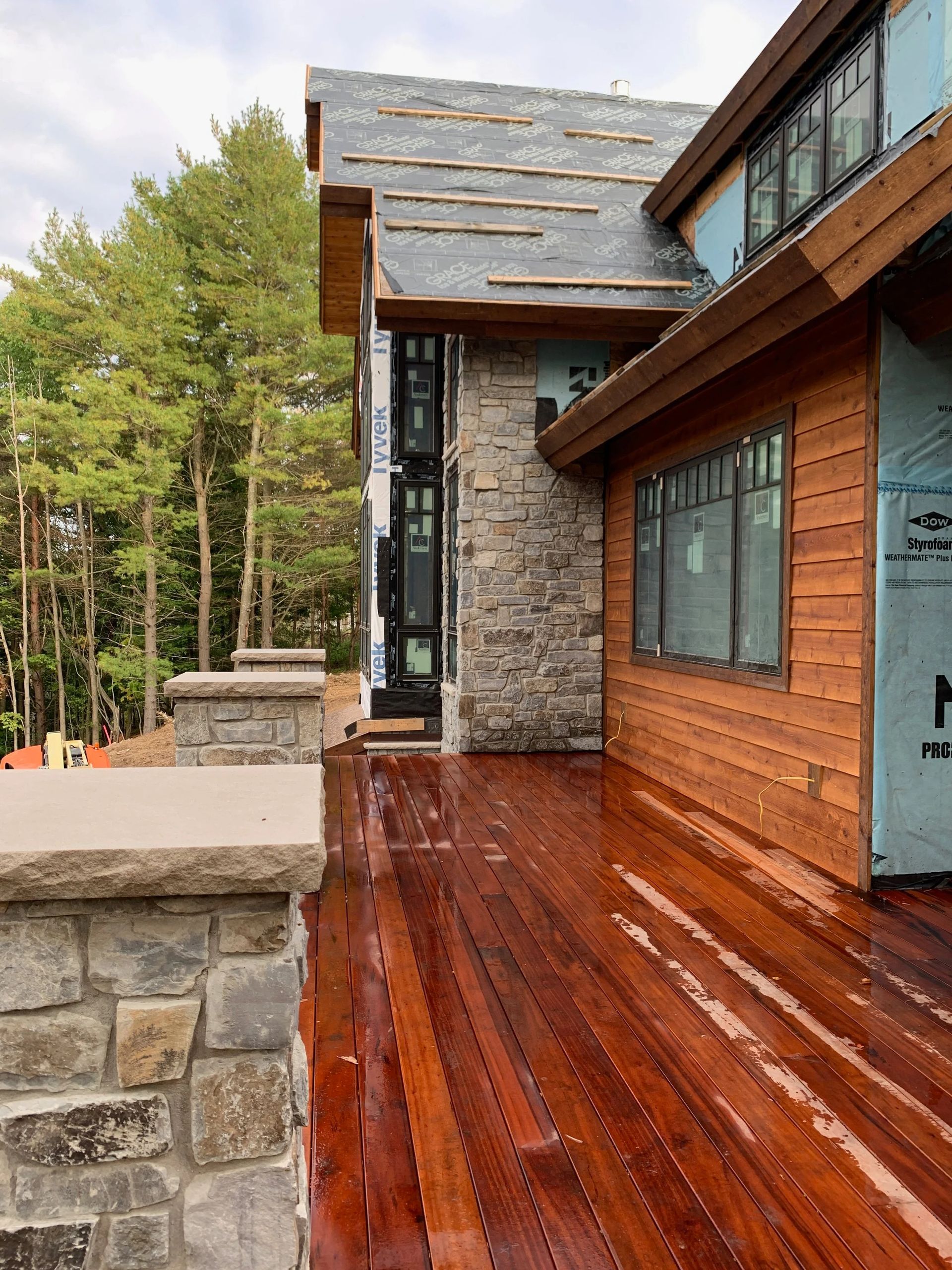 Wooden deck beside a stone-and-wood house, with forest trees in the background.