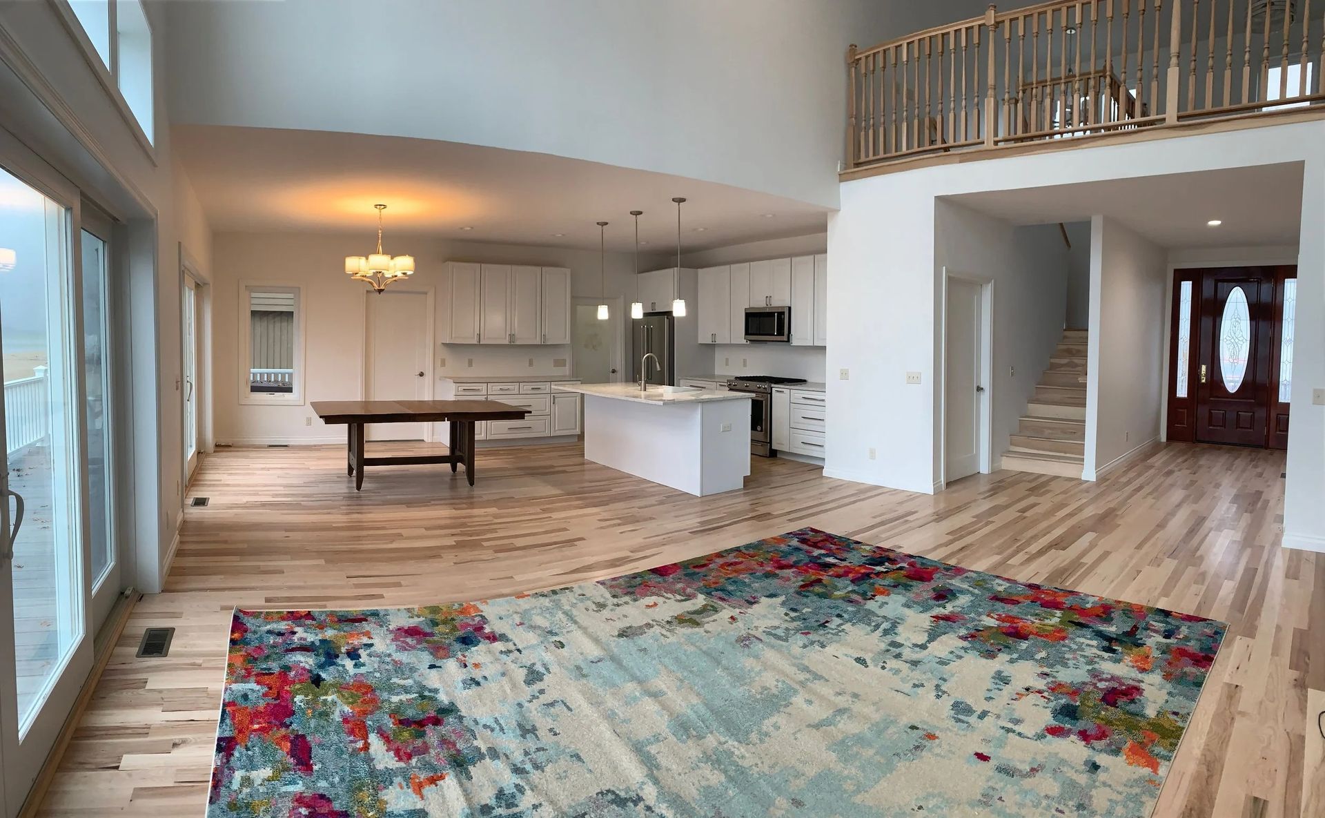 Bright open-concept living room and dining area with vaulted ceiling, white kitchen, and colorful rug