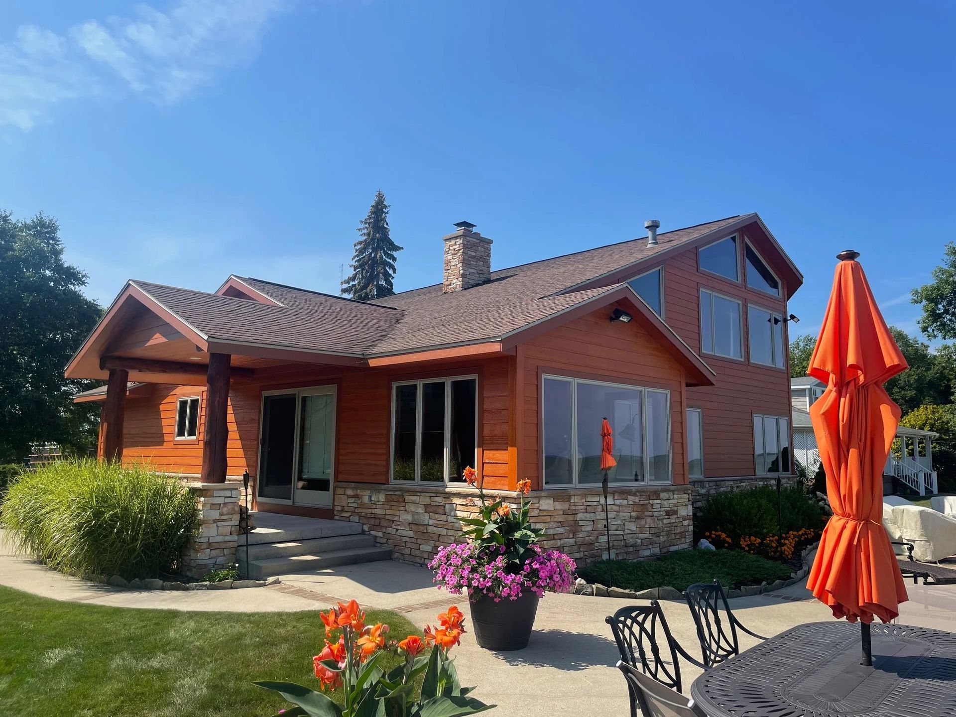 Sunny red house with stone accents, flower beds, and orange patio umbrellas