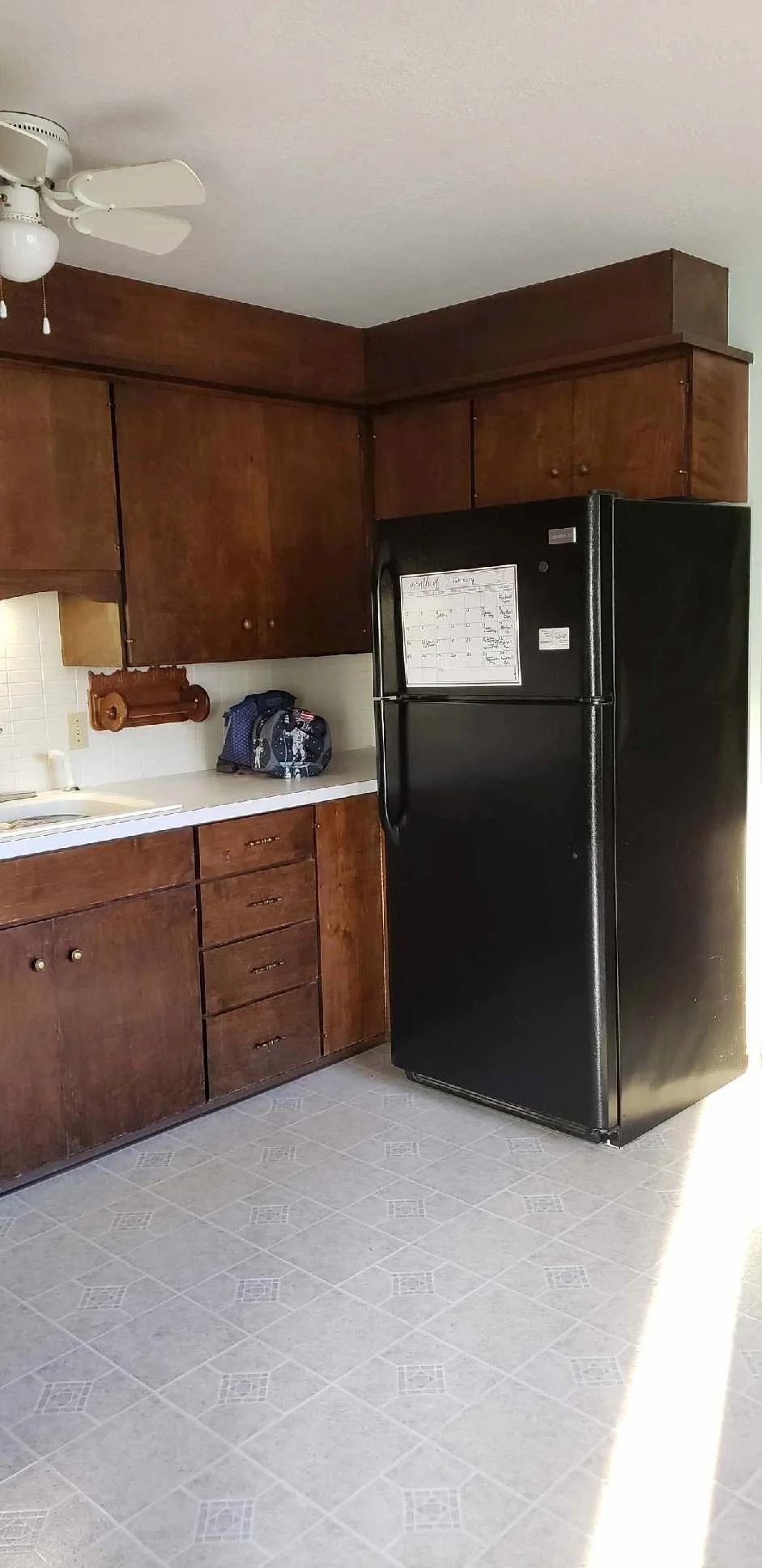Small kitchen with brown cabinets, white tile floor, and a black refrigerator in the corner.