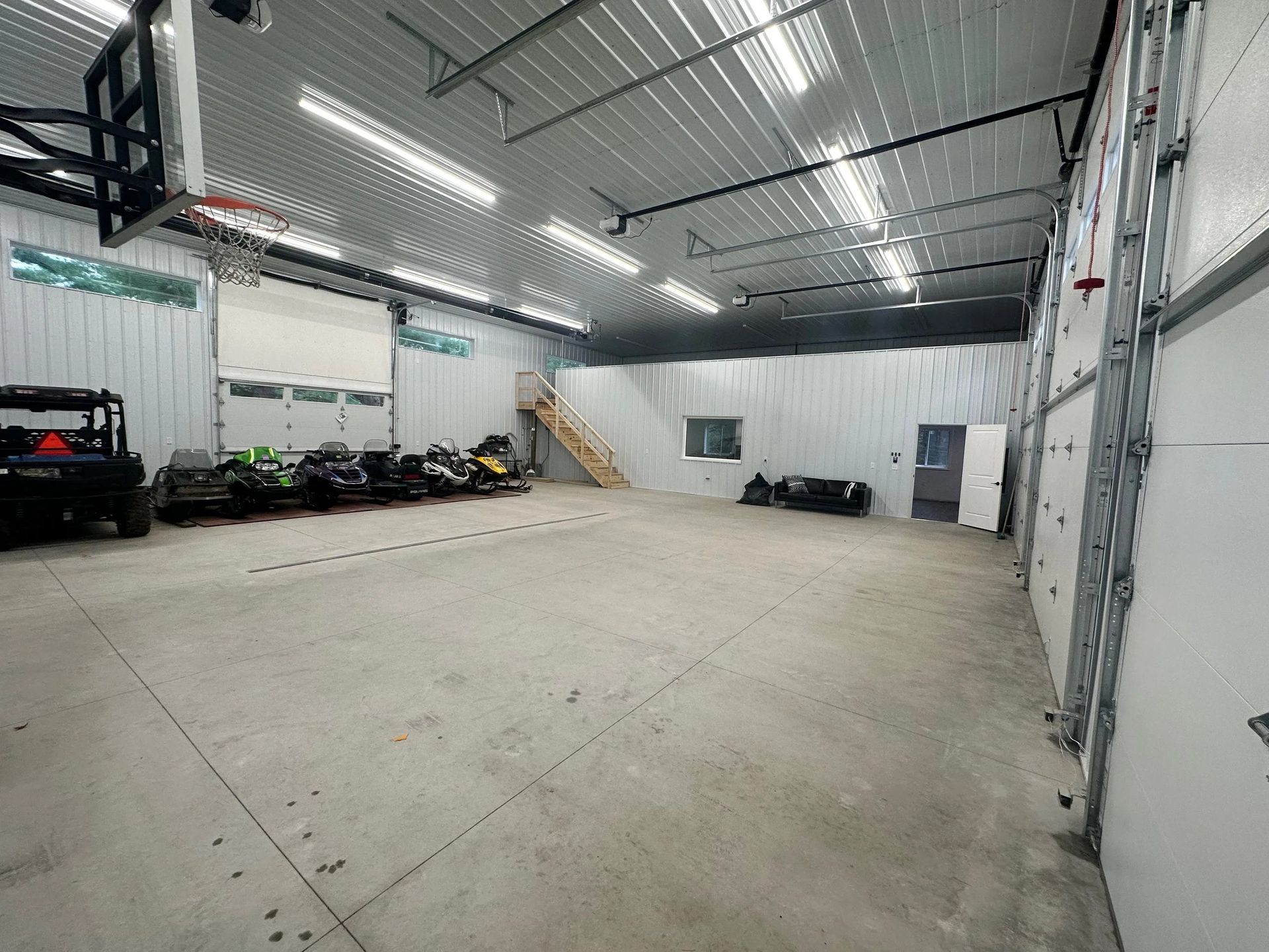 Large empty warehouse with concrete floor, white walls, overhead lights, and a few parked cars along the left wall