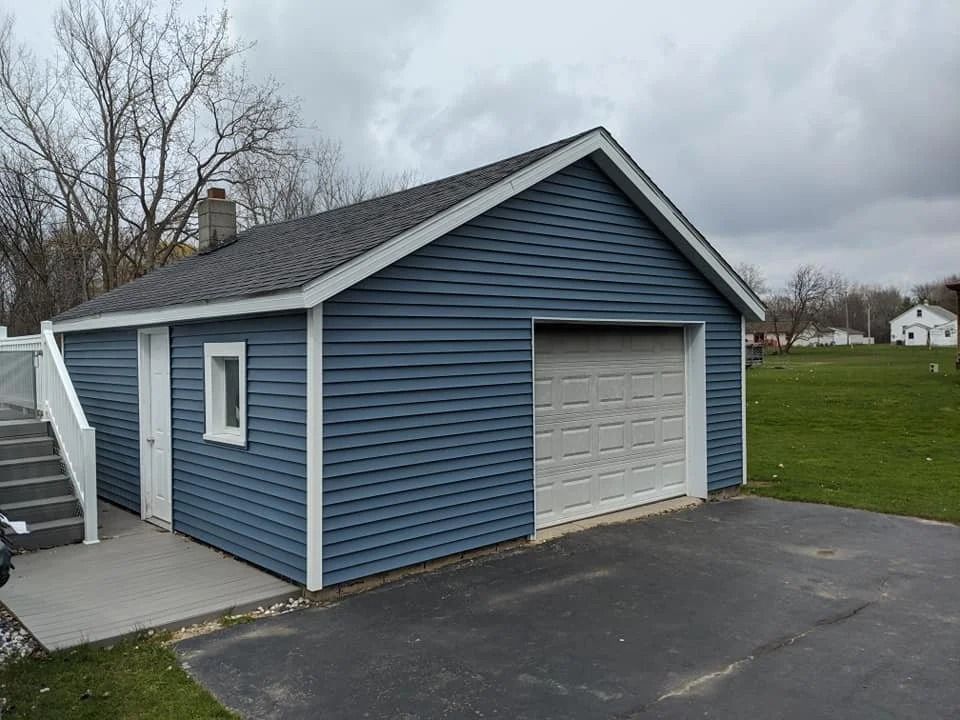 Blue detached garage with white trim and a single door beside an asphalt driveway on a cloudy day