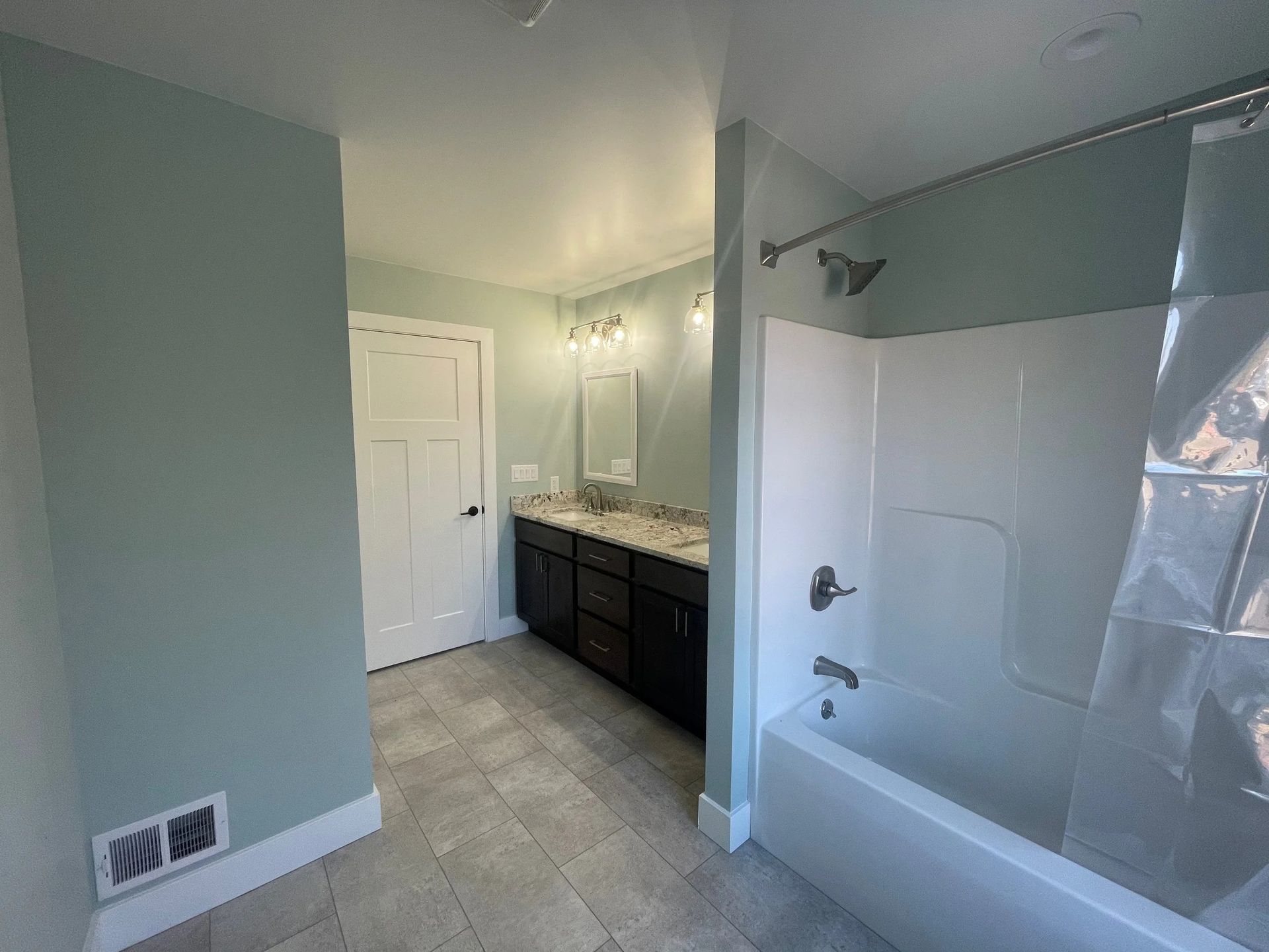 Bathroom with white tub, dark vanity, beige walls, and window light.