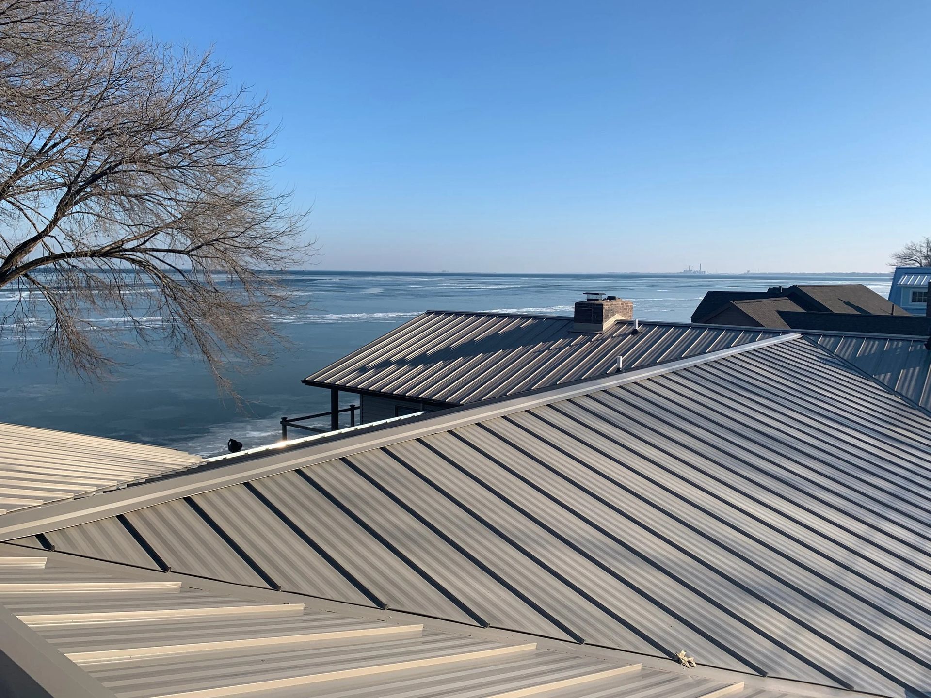 Rooftop overlooking a calm lake under a clear blue sky, with a bare tree at left.