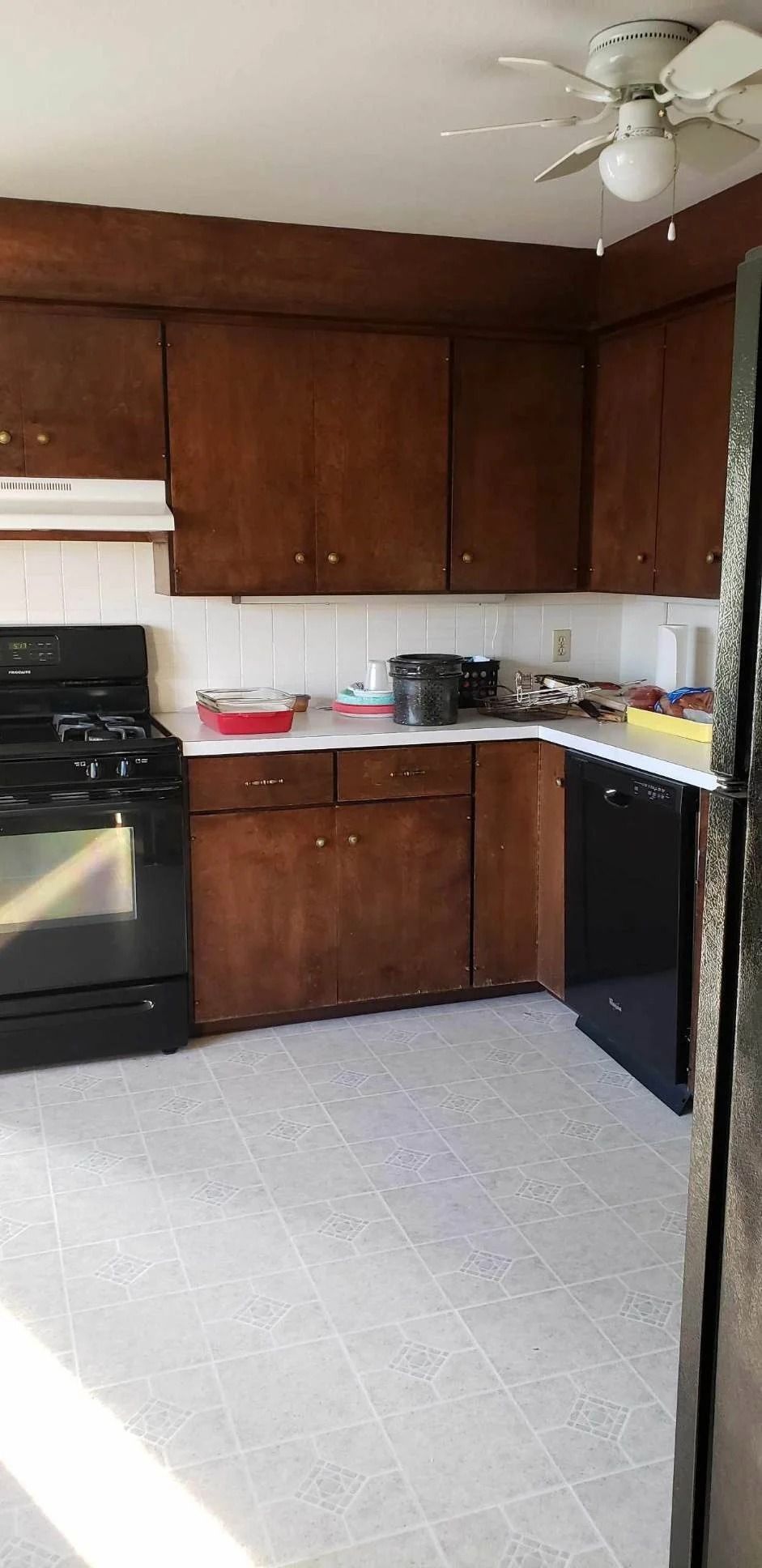 Small kitchen with dark wood cabinets, black stove and dishwasher, white tile floor, and ceiling fan