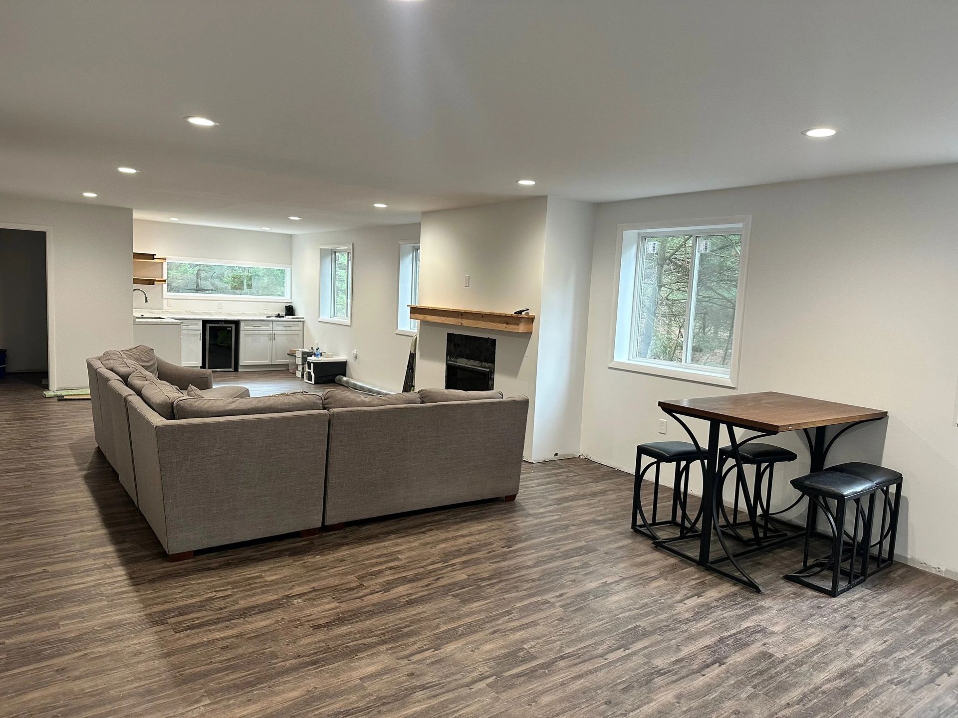 Open-plan living room with gray sectional, fireplace, and small dining table by windows