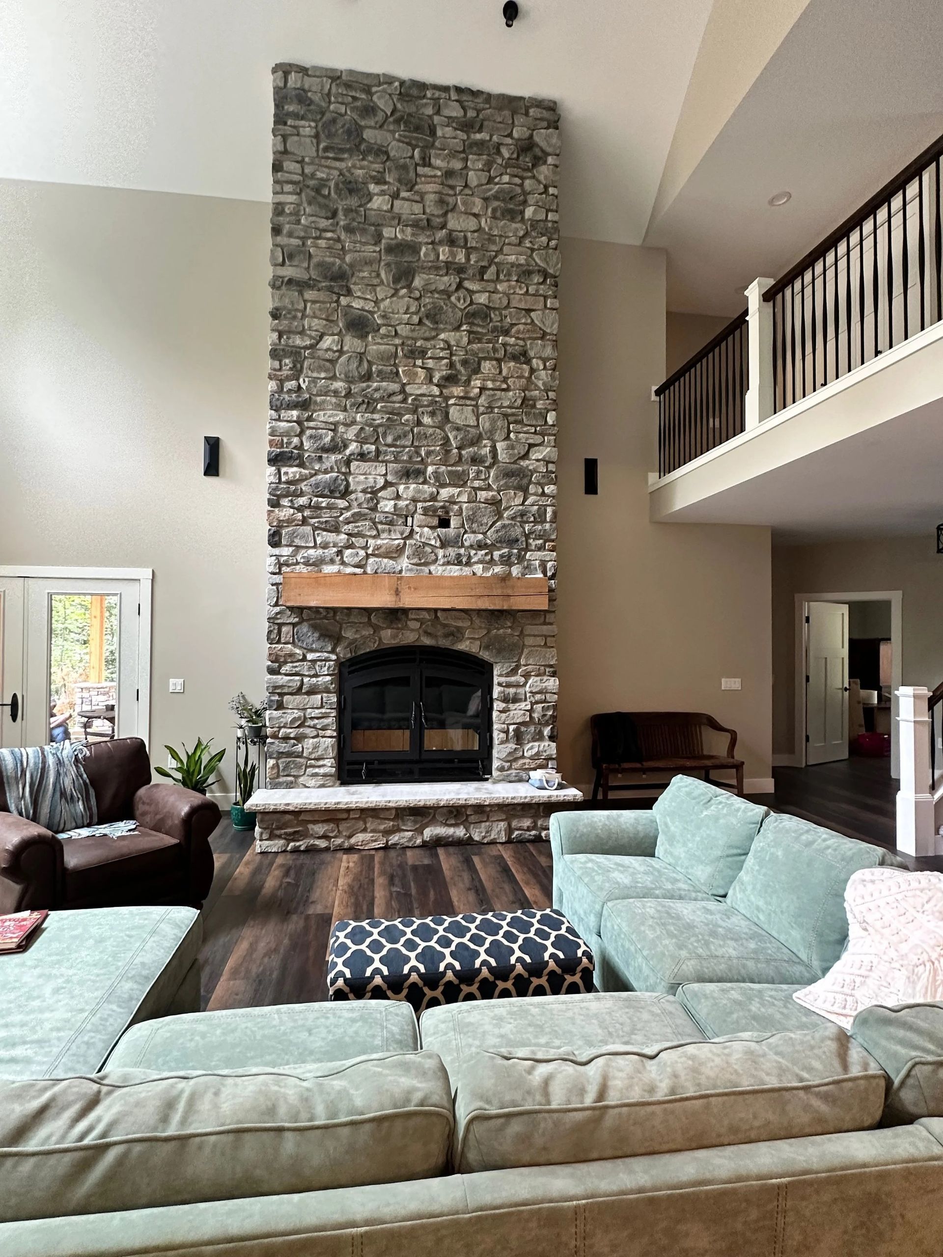 Living room with tall stone fireplace, sectional sofas, and an open loft balcony overhead