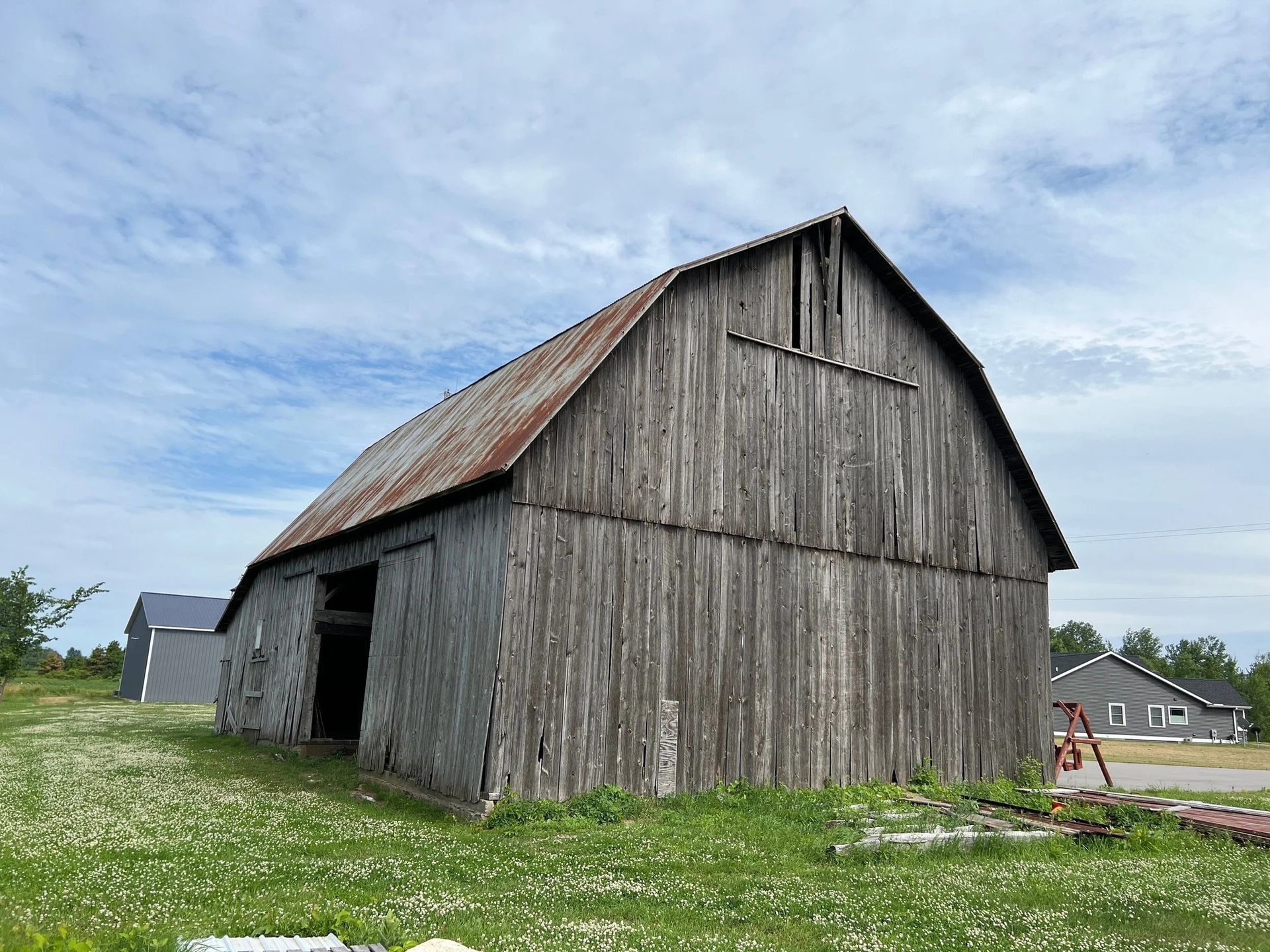 Old weathered wooden barn with a rusted roof in a grassy field under a cloudy sky.