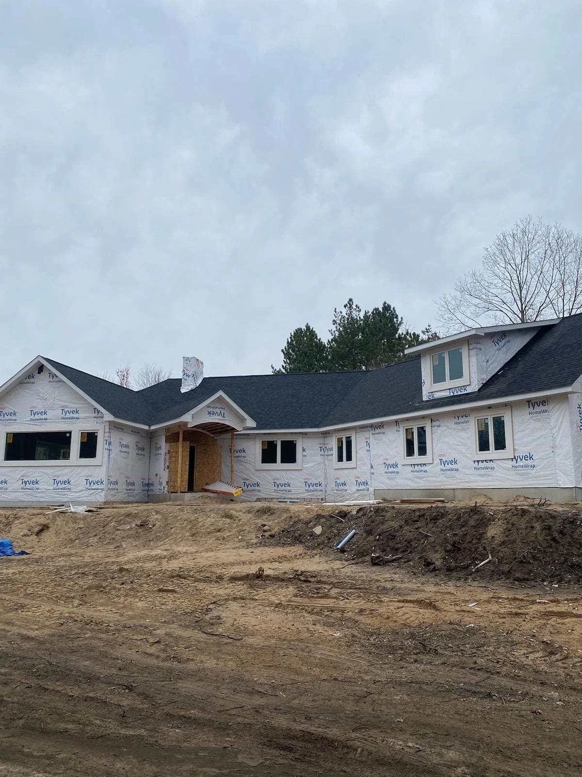 Large unfinished white house under construction with a dirt foreground and cloudy sky
