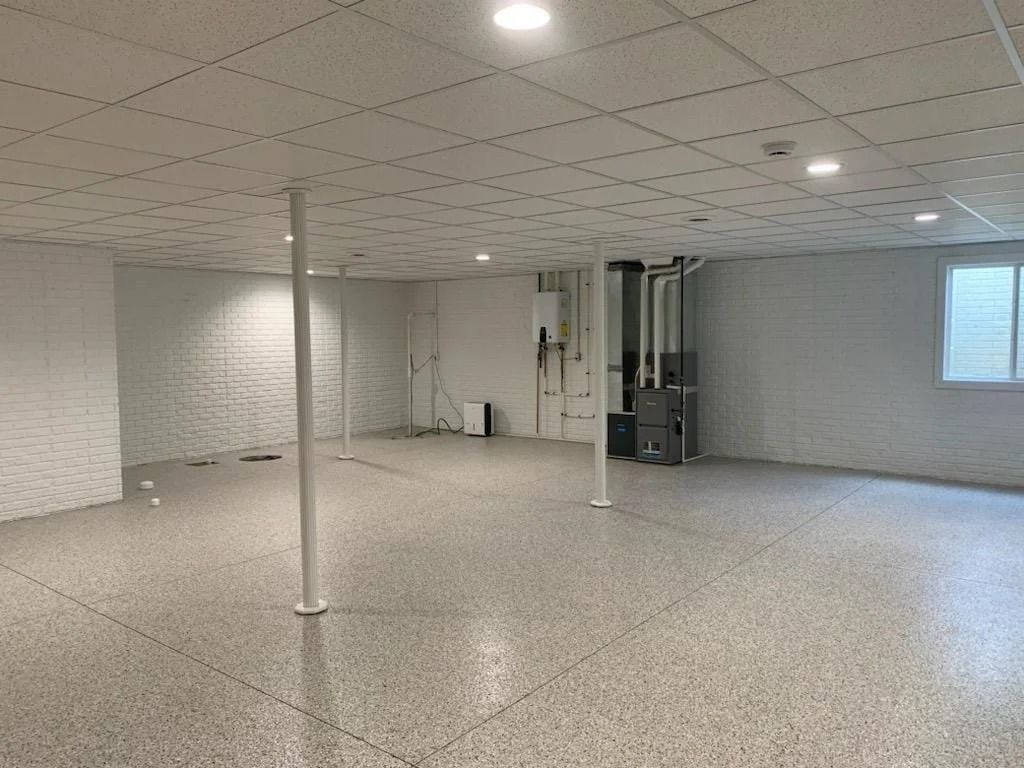 Empty office room with white ceiling tiles, speckled floor, and support columns