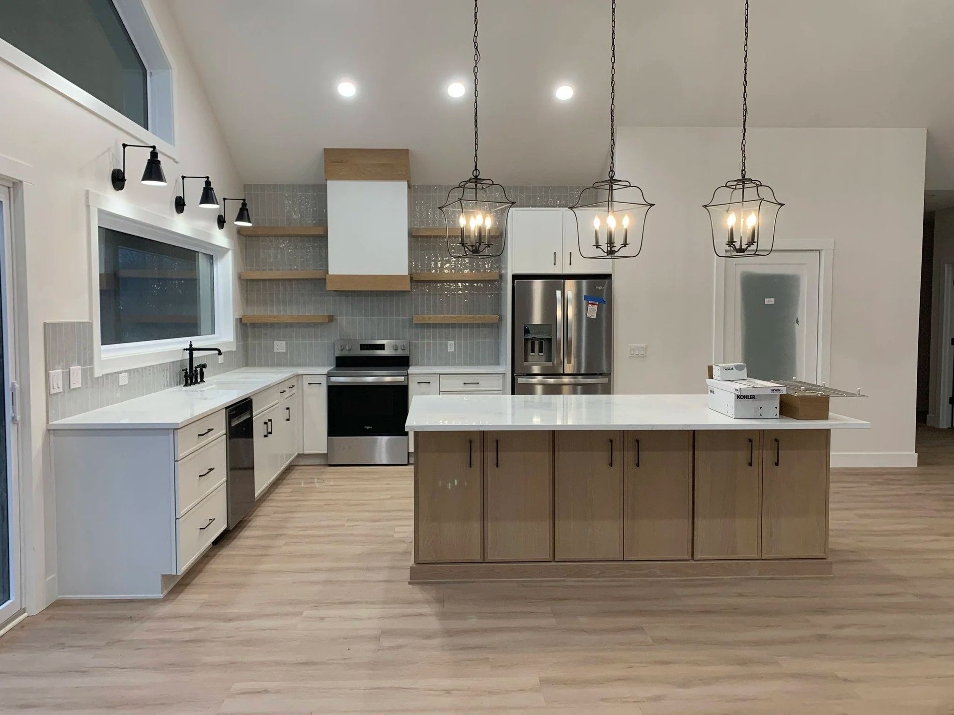 Modern white kitchen with island, stainless appliances, pendant lights, and wood flooring