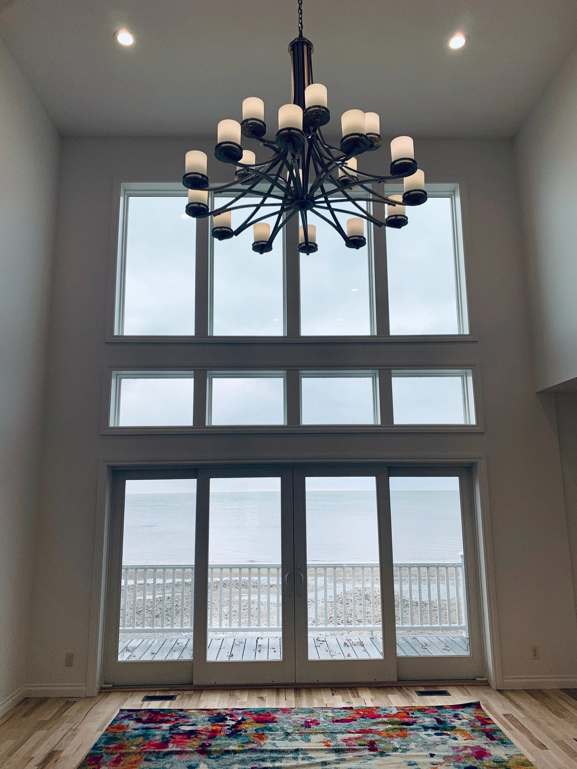 Grand room with tall windows, black chandelier, and patterned rug overlooking water or a distant view