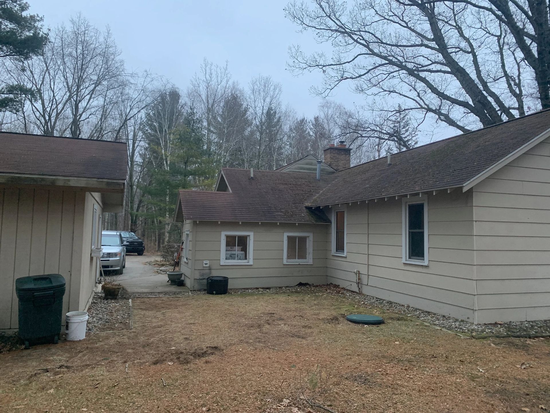 Backyard between beige houses with leaf-covered ground and bare trees under a cloudy sky