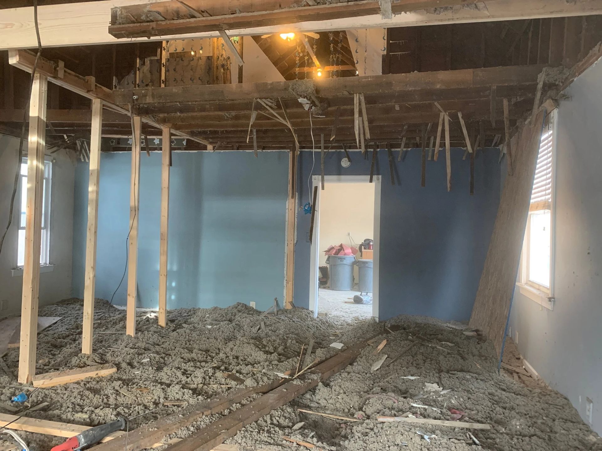 Partially demolished room with exposed ceiling joists, debris-covered floor, and blue walls