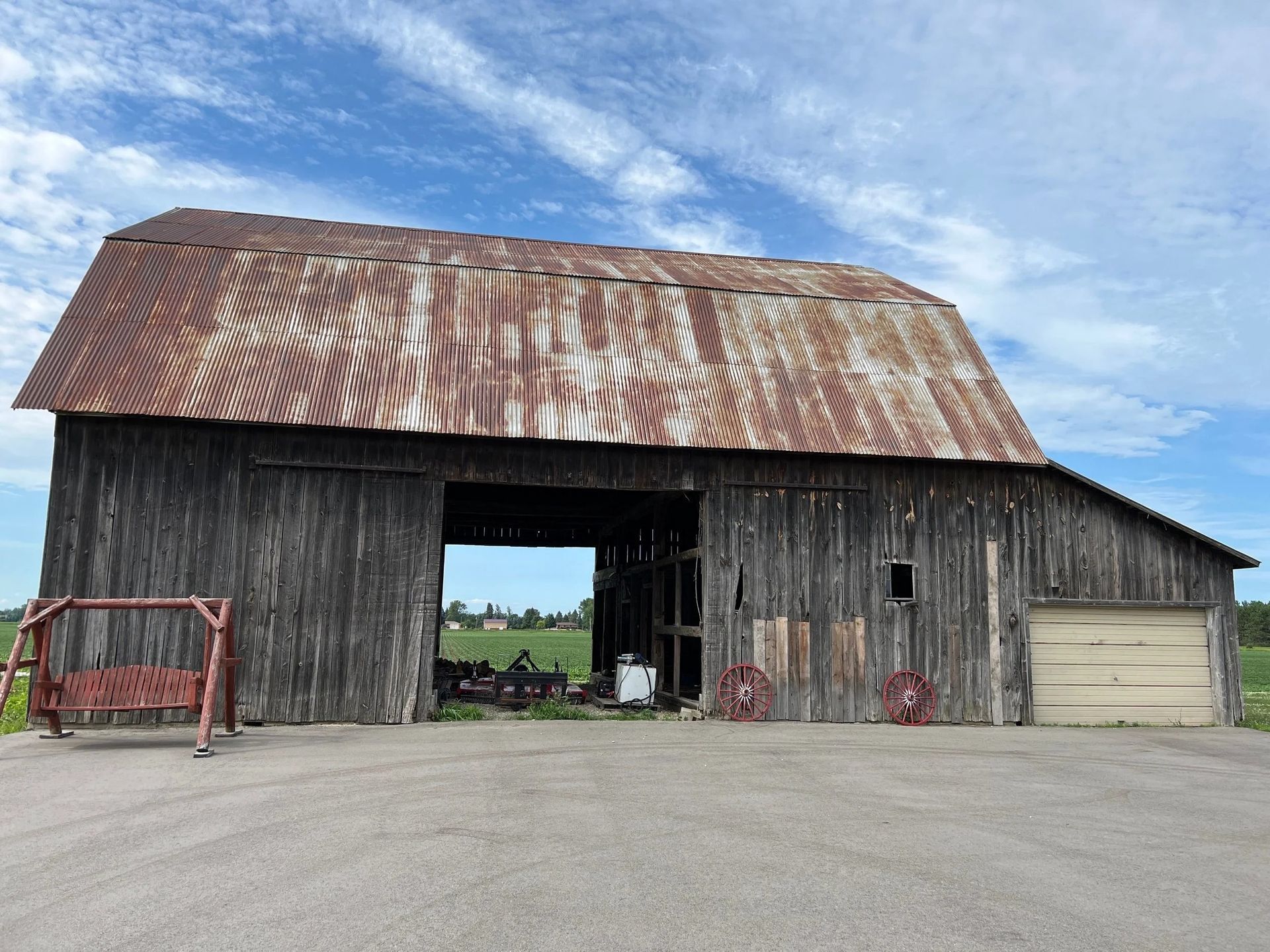 Old weathered barn with rusted roof and open center bay on a farm under a blue sky.