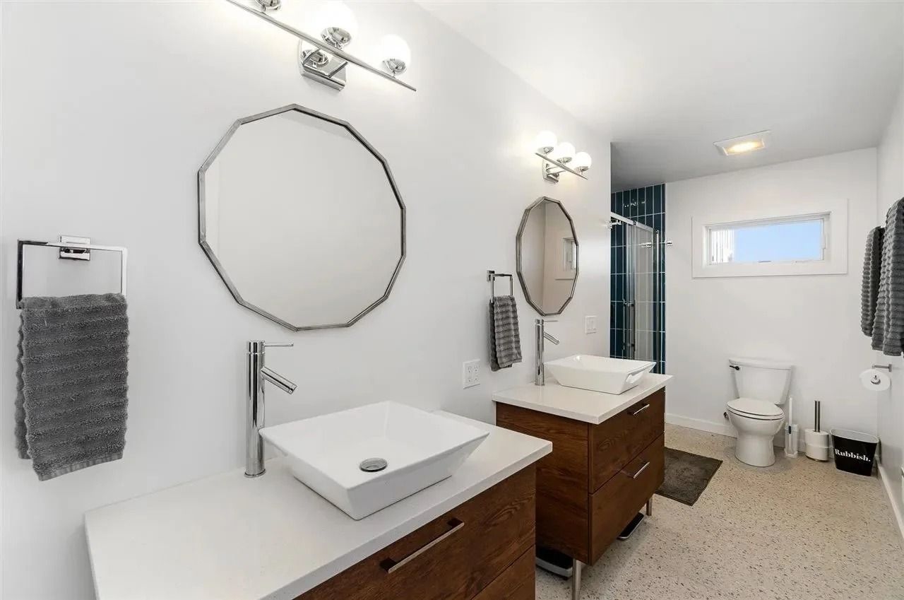 Bright white bathroom with two wood vanities, round mirrors, tiled floor, and a toilet by a small window.