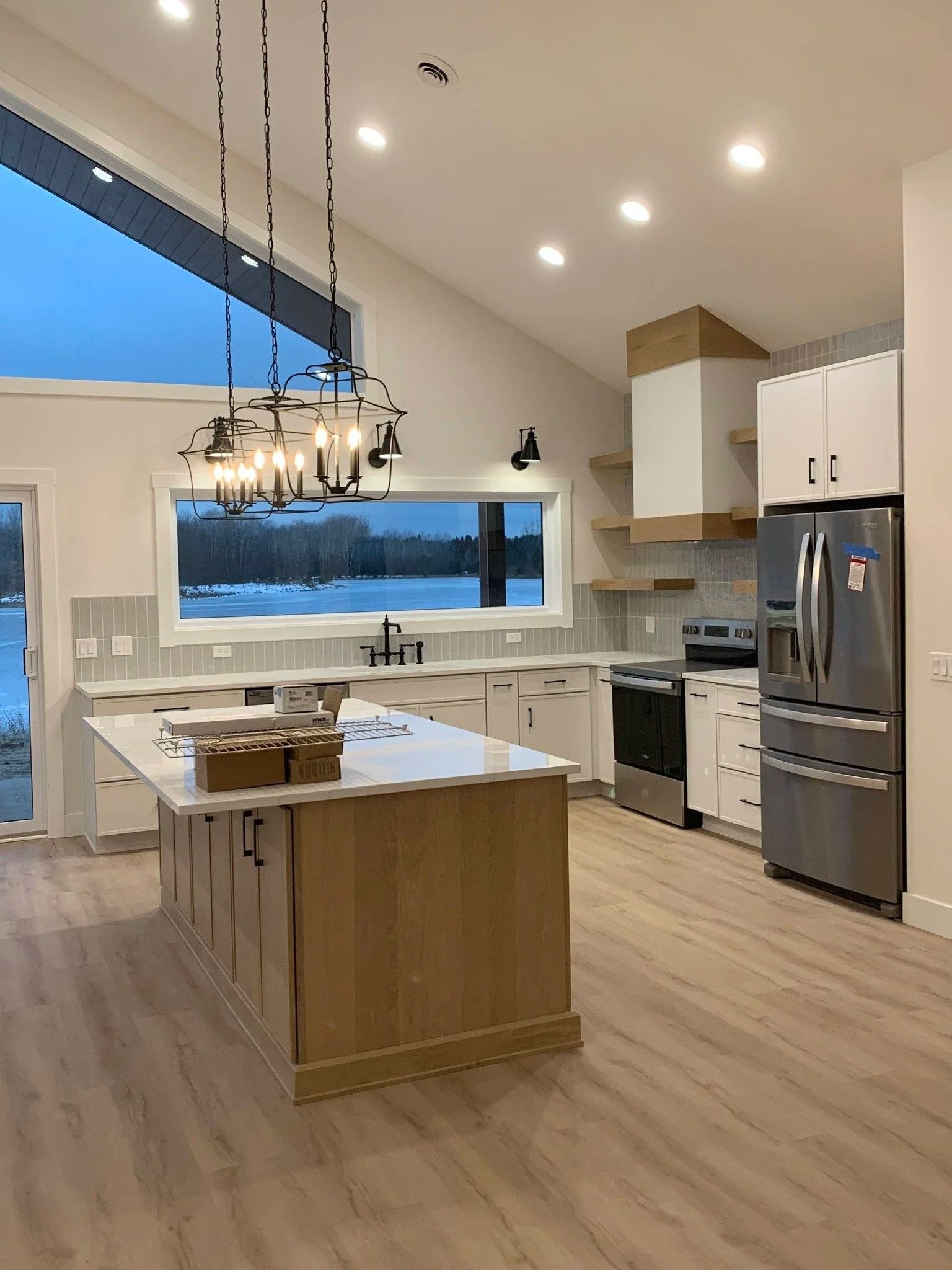 Modern kitchen with island, stainless steel appliances, white cabinets, and large window at dusk