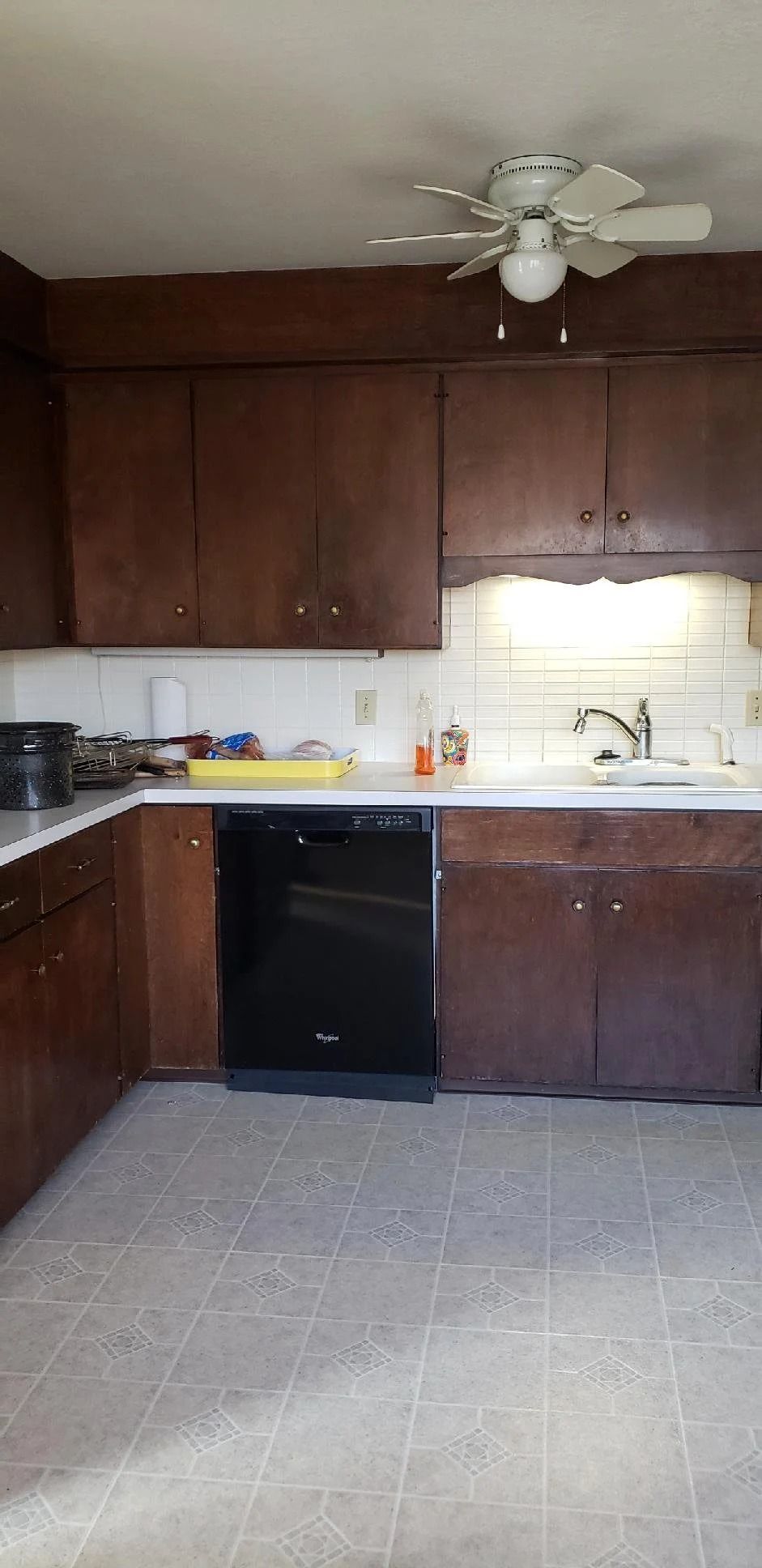 Small kitchen with dark wood cabinets, white backsplash, black dishwasher, and a ceiling fan.