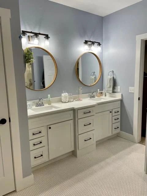 Modern double-sink bathroom vanity with round gold mirrors, gray walls, and white cabinets