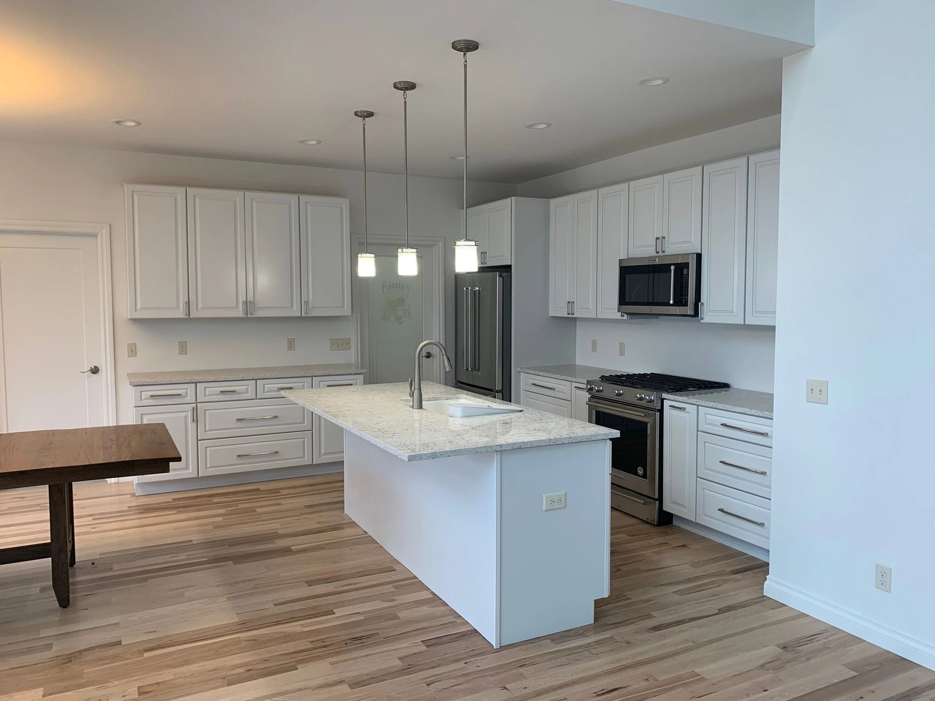 Bright modern kitchen with white cabinets, island, stainless appliances, and wood floors