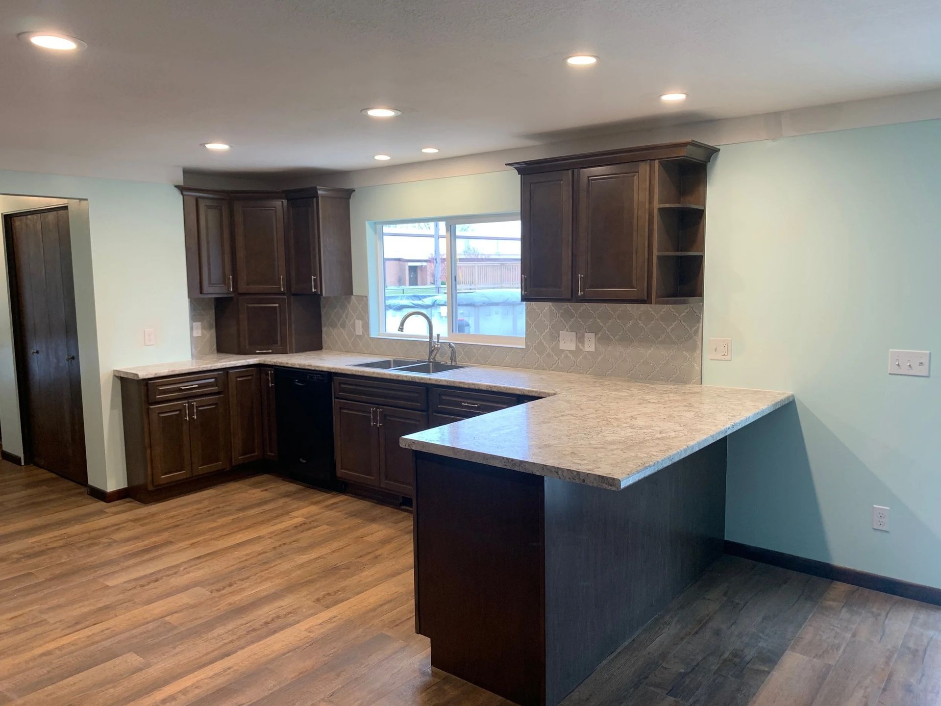 Empty modern kitchen with dark wood cabinets, granite island, and hardwood floors.