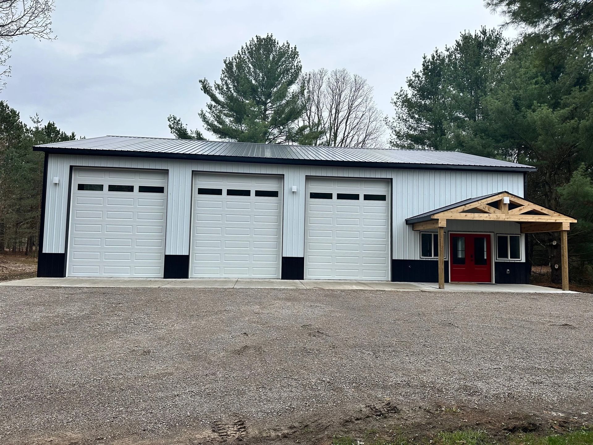 White garage building with three doors and a small red-roofed entrance on a gravel lot