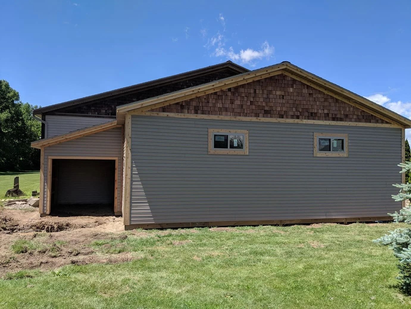 Partially finished house with gray siding, a brick gable, and an open garage under a blue sky