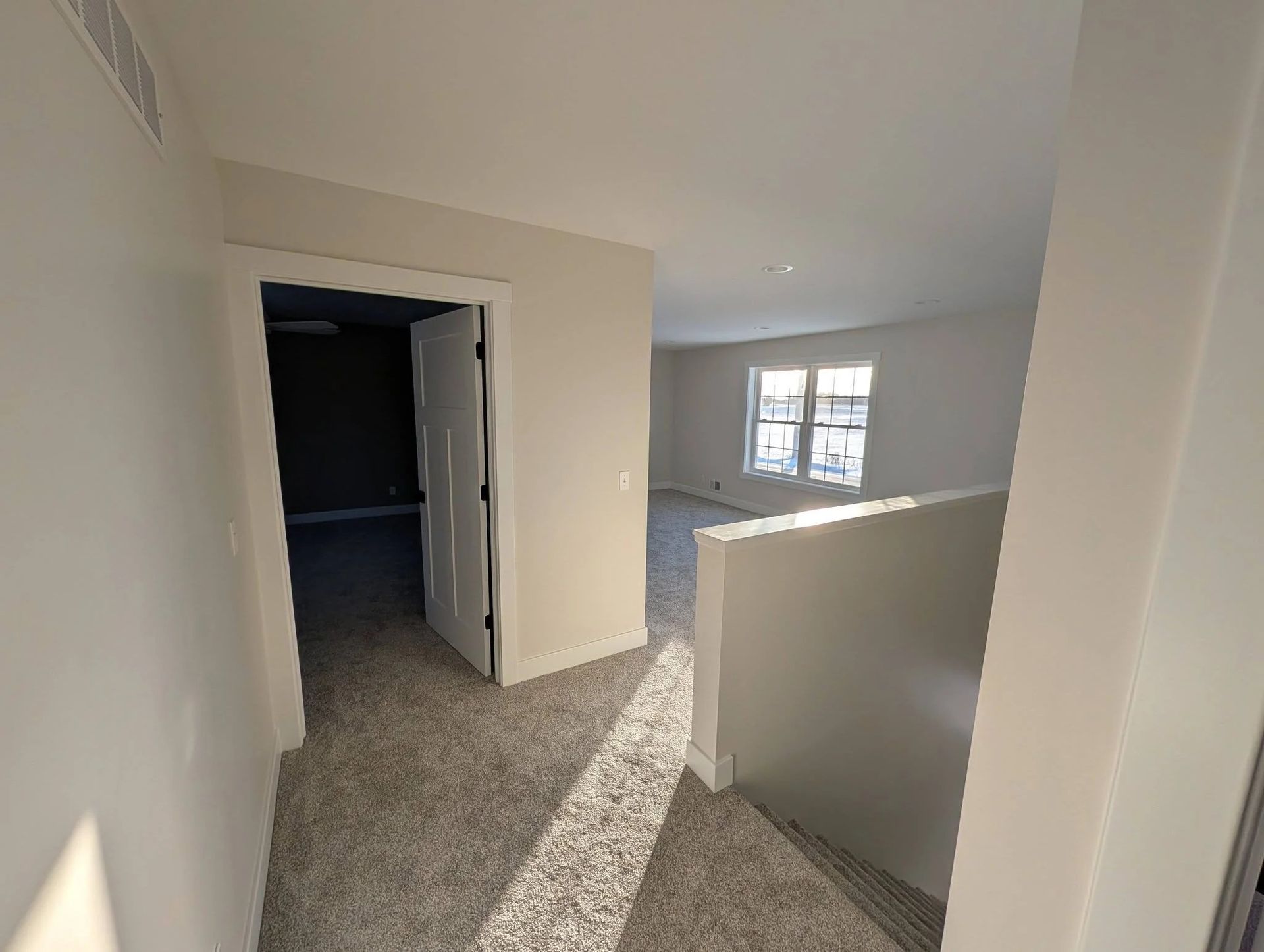 Empty carpeted upstairs hallway with white walls and a window casting light.