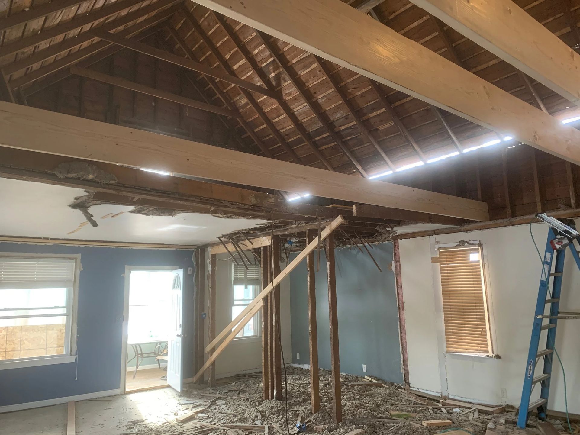 Partially demolished room with exposed roof beams, blue walls, and a ladder leaning against the right wall
